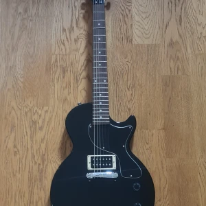 Epiphone Les Paul Junior Elgittar  - Inspirerad av Gibson Collection Kropp i mahogny Hals i mahogny Indisk lagerbräda Vintage 50-tals halsform Skala: 629 mm (24,75") Mutterbredd: 43 mm (1.693") 22 band 1st P-90 Pro Dog Ear single coil pickup 1 Volymkontroll 1 Tonkontroll Lightning Bar Wrap Around bro Vintage Style Deluxe maskinhuvuden Färg: Vintage Sunburst