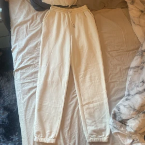 Beige mjukisbyxor från NA-KD - Säljer ett par beige mjukisbyxor från NA-KD med resår och dragsko i midjan. Byxorna har smal passform med resår vid bensluten och är tillverkade i mjuk bomull. Perfekta för en avslappnad stil.