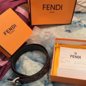 Brunt Fendi bälte med silverfärgat spänne - Säljer ett snyggt bälte från Fendi med klassiskt FF-mönster i brunt och svart. Bältet har ett stort, silverfärgat Fendi-spänne och levereras i originalask. Perfekt accessoar för att lyfta din outfit.