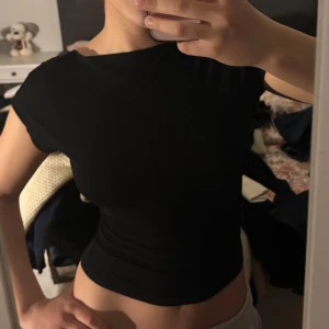 Svart tight topp med öppen rygg - Säljer en svart tight topp med korta ärmar och en snyggt öppen rygg. Perfekt för dig som vill ha en enkel men ändå iögonfallande topp. Passar till många olika stilar och är superbekväm.