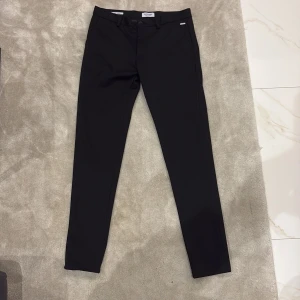 Svarta kostymbyxor från Jack & Jones - Snygga svarta kostymbyxor från Jack & Jones, modell Slim Marco. Byxorna har slim passform, klassiska fickor fram och bak samt bälteshällor. Perfekta för en stilren look.