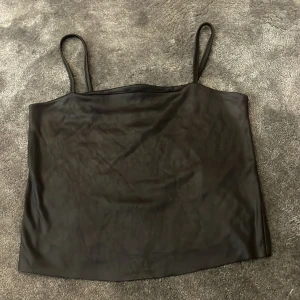 Svart satin linnetopp - Säljer en svart linnetopp i satin med tunna axelband. Toppen har en enkel och stilren design, perfekt att matcha med olika outfits.