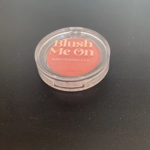 Blush från Makeup Mekka - Säljer en blush i  från Makeup Mekka. Kommer i en rund, genomskinlig plastförpackning med lock. Färgen är en varm, matt rosa-ton som passar perfekt för att ge kinderna en fräsch look.