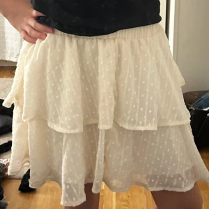 Vit volangkjol med prickigt mönster - Säljer en söt vit kjol med volanger och diskret prickigt mönster. Kjolen är kort och har en luftig känsla med flera lager tyg. Ser genomskinlig ut på bilden men jag upplever att den inte är de! Använd fåtal gånger INGA TECKEN på användning❤️❤️