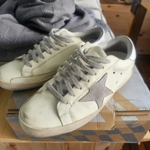 Golden Goose sneakers med grå stjärna - Säljer ett par vita Golden Goose sneakers med grå mockadetaljer och grå snörning. Perfekta för en avslappnad och trendig stil.