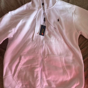 Vit hoodie från Polo Ralph Lauren - Säljer en klassisk vit hoodie från Polo Ralph Lauren med dragkedja och huva. Tröjan har två stora fickor framtill och den ikoniska broderade loggan på bröstet. Perfekt för en avslappnad och stilren look. Det står 3XL fast det passar nog om du har XXL. Pris kan diskuteras