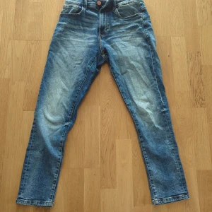 Blå jeans från Smog - Säljer ett par klassiska blå jeans från Smog i storlek 28/30. Jeansen har normal passform, fem fickor och stängs med dragkedja och knapp. Snyggt slitna detaljer, knappt använda, inga hål eller fläckar 