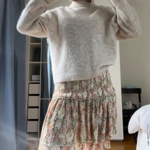 Blommig volangkjol i pastellfärger - Supersöt kjol med blommigt mönster i ljusa pastellfärger. Kjolen har volanger och smock i midjan som ger en bekväm och feminin passform. Perfekt för både vardag och fest i vår och sommar 