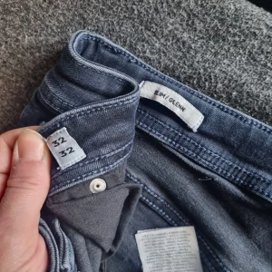 Slim Glenn jeans i mörkblå denim - Mörkblå jeans från Slim Glenn i rak passform. Klassisk femficksmodell med dragkedja och knapp i midjan. Jeansen har ett hål på ena benet för en mer avslappnad look. Perfekta för dig som gillar en enkel och stilren stil. Pris:100kr