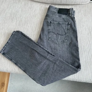 Grå jeansbyxor med rak passform - Snygga grå jeansbyxor med klassisk femficksdesign och rak passform. Byxorna har en enkel bakficka och svart patch vid linningen. Perfekta till vardags för en avslappnad stil.