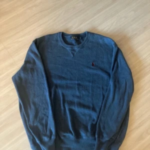 Blå stickad tröja från Polo Ralph Lauren - Mörkblå stickad tröja från Polo Ralph Lauren med rund halsringning och röd broderad logga på bröstet. Klassisk och enkel design som passar till mycket. Mjuk och skön kvalitet.