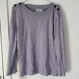 Ljuslila tröja med knappar från Alice Bizous - Säljer en ljuslila långärmad tröja från Alice Bizous. Tröjan har rund halsringning och dekorativa svarta knappar på axlarna. Tillverkad i mjukt material, perfekt för svalare dagar💕