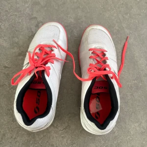 Vita sneakers från SOC - Säljer ett par vita sneakers från SOC med rosa snören och detaljer samt bruna sulor. Skorna har meshpaneler för extra ventilation och svart innerfoder. Perfekta för träning eller vardag.