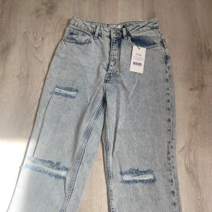 Ljusblå jeans med slitningar  - Säljer ett par ljusblå jeans från Gina Tricot med slitna detaljer på benen och råa, fransiga benslut. Jeansen har normal passform. Helt oanvända med prislapp kvar.