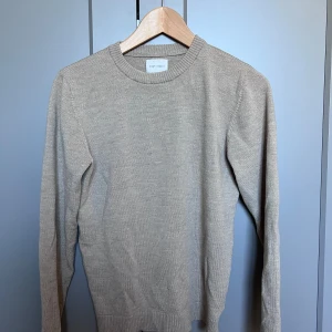 Beige stickad tröja från A Day's March - Säljer en stilren beige stickad tröja från A Day's March i merinoull. Tröjan har rund halsringning och långa ärmar, perfekt för lager-på-lager. Enkel och klassisk design som passar till mycket.