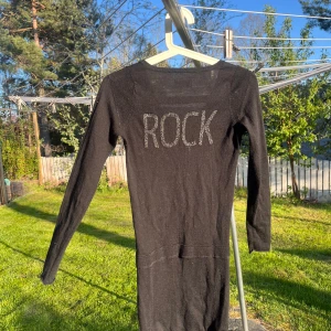 Svart klänning med texten ”Rock”  från Zadig & Voltaire - Svart långärmad klänning från Zadig & Voltaire med v-ringning framtill och texten 'ROCK' i grått på ryggen. Klänningen har en tight passform och är perfekt för dig som gillar en stilren look med attityd! Meddela gärna om du har fler frågor💗