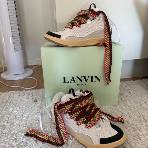 Lanvin sneakers med färgglada snören - Säljer ett par Lanvin sneakers i vitt och svart med beige sula och riktigt breda, färgglada snören i rött, gult och grönt. 