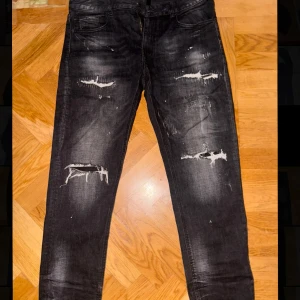 Svarta slitna jeansbyxor - Svarta jeans med slitningar och blekta detaljer framtill. Klassisk femficksmodell med dragkedja och knapp. Jeansen har en rak passform och är perfekta för en avslappnad stil.