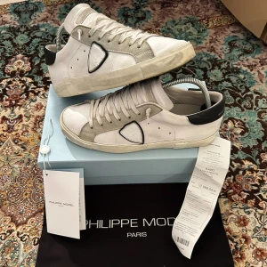 Philippe Model sneakers i vitt och grått - Säljer ett par Philippe Model sneakers i vitt skinn med grå mockadetaljer och svart häl. Klassisk design med snörning och rund tå. Kommer med originalkartong, dustbag och kvitto. Perfekta för dig som gillar stilrena och exklusiva sneakers.