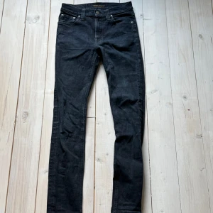 Svarta jeansbyxor från Nudie Jeans - Säljer ett par svarta jeansbyxor från Nudie Jeans med klassisk femficksdesign och raka ben. Jeansen har normal passform och är tillverkade i ett mjukt bomullsmaterial. Perfekta för dig som gillar stilrena och tidlösa jeans.