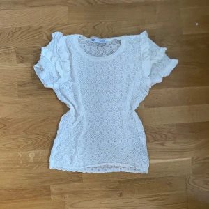 Vit spetsblus med volangärmar  - Säljer en söt vit blus från zara med spetsmönster och volangdetaljer på ärmarna. Blusen har rund halsringning och korta ärmar, perfekt för en fräsch och somrig look.