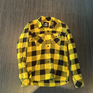 Gul och svart rutig skjorta från Dickies - Säljer en snygg gul och svart rutig skjorta från Dickies i storlek XS. Skjortan har långa ärmar, klassisk krage och två bröstfickor med knappar. Perfekt för dig som gillar streetwear och vill sticka ut lite extra.
