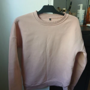 Ljusrosa sweatshirt - Säljer en ljusrosa sweatshirt med rund halsringning och ribbade muddar. Tröjan är enkel och stilren, perfekt för en avslappnad look. Mjuk insida för extra komfort.