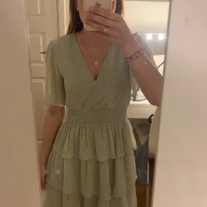 Somrig grön klänning med volanger - Grön smockad klänning med volanger från NA-KD! Stretchigt tyg vid midjan så den sitter bra. Jätte luftig och skön. Använd en gång.