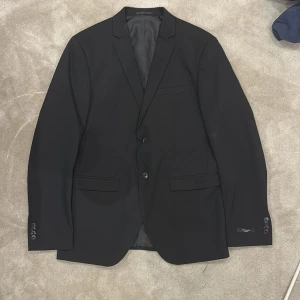 Svart kostym från Jack & Jones Premium  - Säljer en svart kostym från Jack & Jones Premium i super slim passform. Kavajen har två knappar framtill, tre knappar vid ärmslut och klassiska fickor. Byxorna är raka och stilrena och slimfit. Perfekt för bal eller fest.