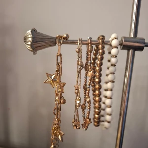 Set med armband i guld och vitt med stjärndetaljer - Säljer ett set med fem armband i olika stilar. Två guldiga armband med stjärnberlocker, ett guldigt pärlarmband, ett vitt pärlarmband och ett armband med små guldstjärnor och pärlor. Perfekt för att mixa och matcha till din stil. De är lite rostade och en är brunguld inte gulguldig. Därav billigt pris💗