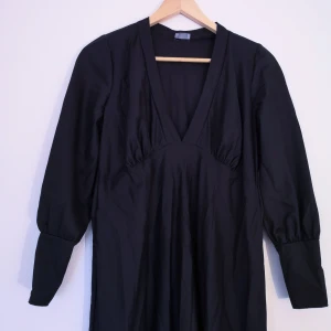 Svart klänning strl S - Svart klänning med vackra detaljer, sitter bäst på dig med större byst för kuporna var för stora på mig som har rätt liten byst. Längd från axel 125cm, bredd under bysten 84cm. Kan fixa fler bilder och mått vid intresse!  Obs, är bara lite damm som syns på en av bilderna inte en fläck, jag såg det inte när jag tog kort. 