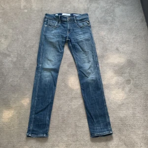 Blå jeansbyxor med raka ben - Säljer ett par klassiska blå jeansbyxor med raka ben och fem fickor. Byxorna har dragkedja och knapp framtill samt en läderpatch bak i midjan. Perfekta för en avslappnad stil.