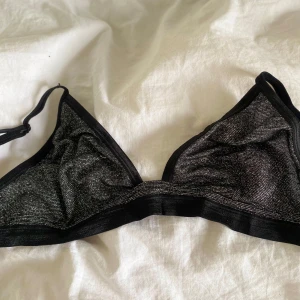 Svart glittrig triangeltopp - Säljer en svart triangelformad topp med glittrigt tyg och tunna axelband. Perfekt för att addera lite extra till din outfit. Toppens material är mjukt och följsamt.