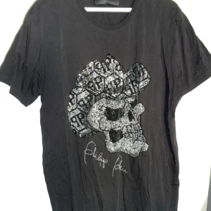 Philipp Plein - Cool svart t-shirt från Philipp Plein med en stor dödskalle framtill, dekorerad med glittriga paljetter och mönster. T-shirten har korta ärmar och rund hals.