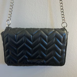 Svart axelväska  - Snygg svart axelväska med quiltat mönster och kedjerem. Väskan har en praktisk storlek och är lätt att bära med sig. Från pull and bear💕