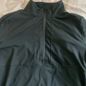 Svart långärmad tröja med halv dragkedja - Svart långärmad tröja med hög krage och halv dragkedja framtill. Perfekt för lager-på-lager och enkel att matcha med olika outfits. Materialet känns mjukt och stretchigt. 