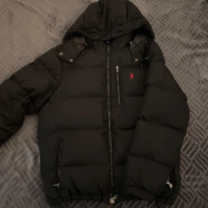 Svart dunjacka från Polo Ralph Lauren - Kan BYTA OXÅ!!  ÄKTA, använd några gånger, säljer för att den är för stor.Från Boozt.  Sista bild är ficka på insidan av jackan. Några frågor? Skriv direkt! Pris kan diskuteras! Väldigt lågt pris pga av efterfrågan.