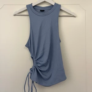 Sommar topp - Babyblå sommar topp från Gina tricot, finns inte längre i sortimentet. Finns en öppning vid midjan med snören så att man kan justera hur tajt man vill att toppen sitter åt. Har inte kommit till så stor användning.