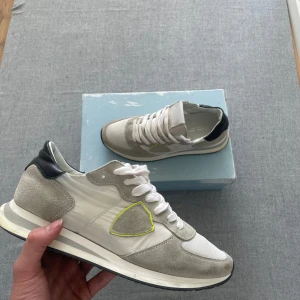 Vita och grå sneakers från Philippe Model trpx - Säljer ett par snygga sneakers från Philippe Model i vitt och ljusgrått med detaljer i mocka och en gul kant på sidan. Skorna har snörning, svart häl och en platt sula. Perfekta för en stilren vardagslook. Ny pris: 3500kr mitt pris 1499kr men det är diskuterbart 