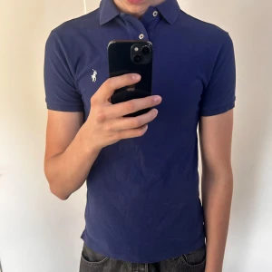 Mörkblå piké t-shirt från Ralph Lauren - Säljer en mörkblå piké t-shirt från Ralph Lauren med klassisk krage och knappslå. Ikoniska broderade loggan i vitt på bröstet. Perfekt basic till garderoben. Använd men bra skick 👍 S slimfit 
