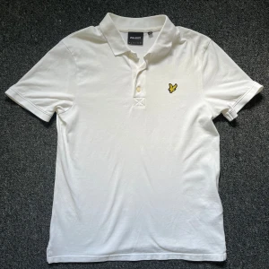 Vit piké t-shirt från Lyle & Scott - Klassisk vit piké t-shirt från Lyle & Scott med gul broderad logga på bröstet. T-shirten har krage och två knappar framtill. Perfekt för en stilren och enkel look. Storlek S och i nytt skick då den annvänd endast 2 gånger. Hör av er vid frågor eller funderingar!