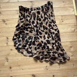 Leopardmönstrad omlottkjol från Zaful - Säljer en snygg leopardmönstrad omlottkjol från Zaful. Kjolen har volangdetaljer och dragkedja i sidan. Den är i ett glansigt, lätt material och har en asymmetrisk form som ger en cool look.