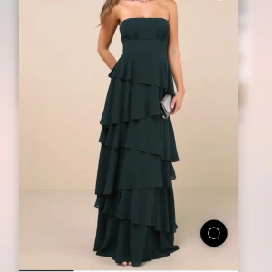Mörkgrön axelbandslös långklänning med volanger - (Intressekoll då jag inte bestämt om jag vill sälja den) elegant mörkgrön långklänning med flera lager volanger och axelbandslös design. Perfekt för bal eller fest. Klänningen har en figurnära passform upptill och faller snyggt ner mot golvet. Helt oanvänd med lapp kvar. Original pris: 1300 från Lulus. Kan både skicka och mötas. Skriv för fler bilder! 