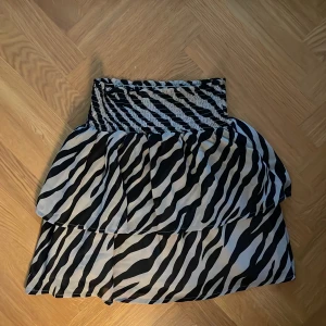 Zebramönstrad kjol från ONLY - Säljer en snygg svartvit zebramönstrad kjol från ONLY i storlek 34. Kjolen har smock i midjan och två volanger. 