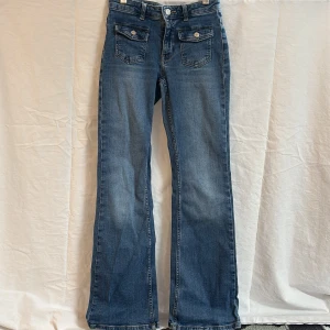 Blå bootcut jeans med fickdetaljer - Snygga blå jeans med bootcut passform och framfickor med lock och silverfärgade knappar från Kappahl storlek 158