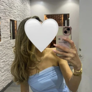 Ljusblå axelbandslös kortklänning - Säljer en ljusblå axelbandslös klänning med draperad detalj och asymmetrisk volang på sidan. Klänningen har en figurnära passform och är perfekt för dig som vill sticka ut med en elegant och modern look.