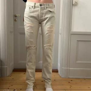 Ljusbeige slitna jeans från Ralph Lauren - Ljusblå/vita jeans från Ralph Lauren med raka ben och slitna detaljer framtill. Låg midja och knappgylf. Oanvända.
