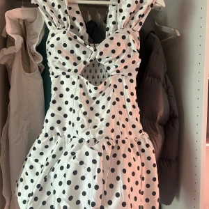 Vit kort prickig klänning med cutout - Supersöt vit kort klänning med svarta prickar, klänningen har en cutout-detalj framtill. Går att ha off shoulder!!