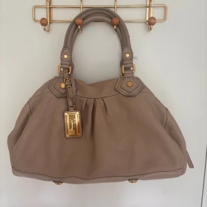 Beige handväska Marc by Marc Jacobs - Säljer denna fina väska från Marc by Marc Jacobs då den ej kommer till användning. I fint skick, en defekt syns på sista bilden men det märks knappt. Modellen Q classic baby groov.