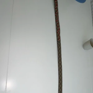 Gucci GG Snake bälte - Snyggt Gucci-bälte i beige och brunt GG Supreme-mönster med detaljer av röda ormar. Spännet är i guldtonad metall och bältet är gjort i skinn. Perfekt accessoar för att lyfta din outfit med lyxig känsla och cool design.